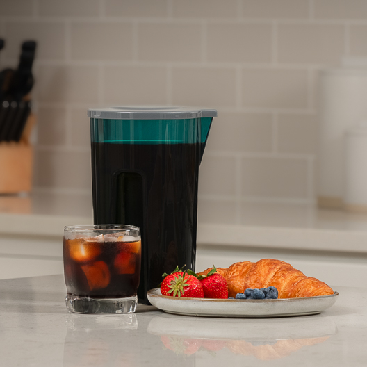 Toddy Essential Pitcher Blue with a Cold Brew Coffee drink and a plate of food on a kitchen counter