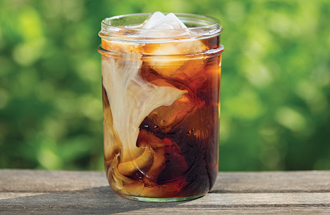 glass of cold brew coffee served over ice with milk on a table outside